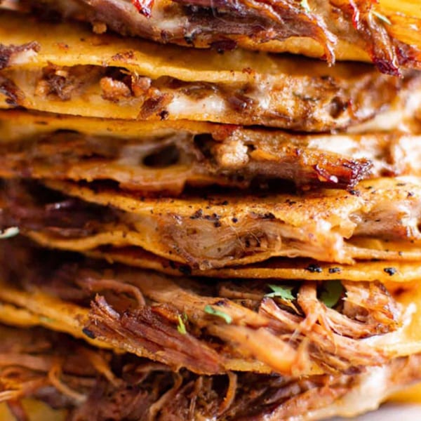 Close-up of a stack of MissTakoz birria quesadillas with melted cheese and shredded beef.
