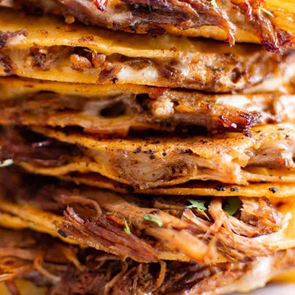Close-up of a stack of MissTakoz birria quesadillas with melted cheese and shredded beef.