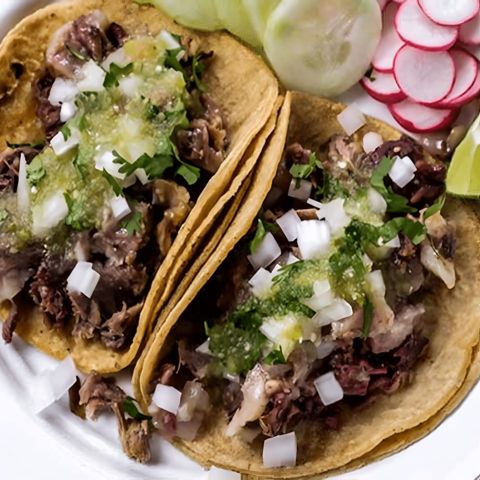 Two MissTakoz tacos with meat, onions, cilantro, and green salsa, served with radishes and lime.