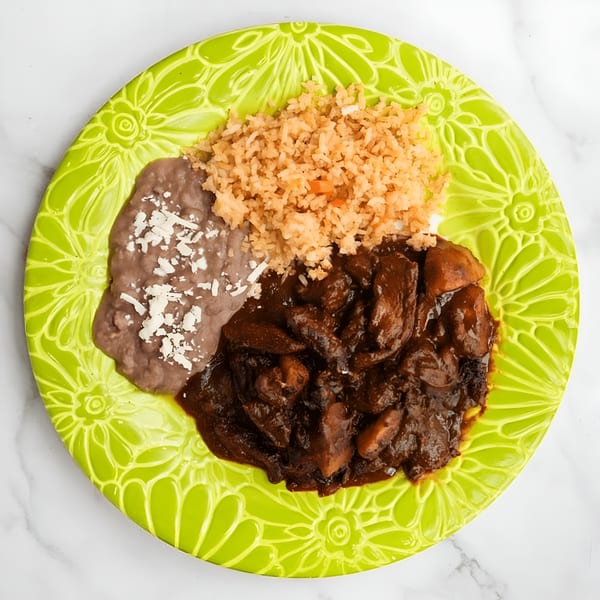 MissTakoz Mexican dish with mole, rice, and refried beans on a bright green plate.