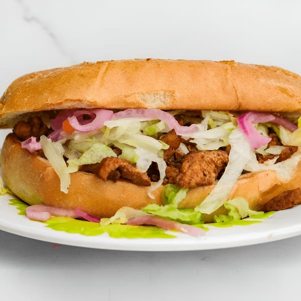 A MissTakoz Mexican torta, filled with meat, shredded lettuce, and pickled red onions.